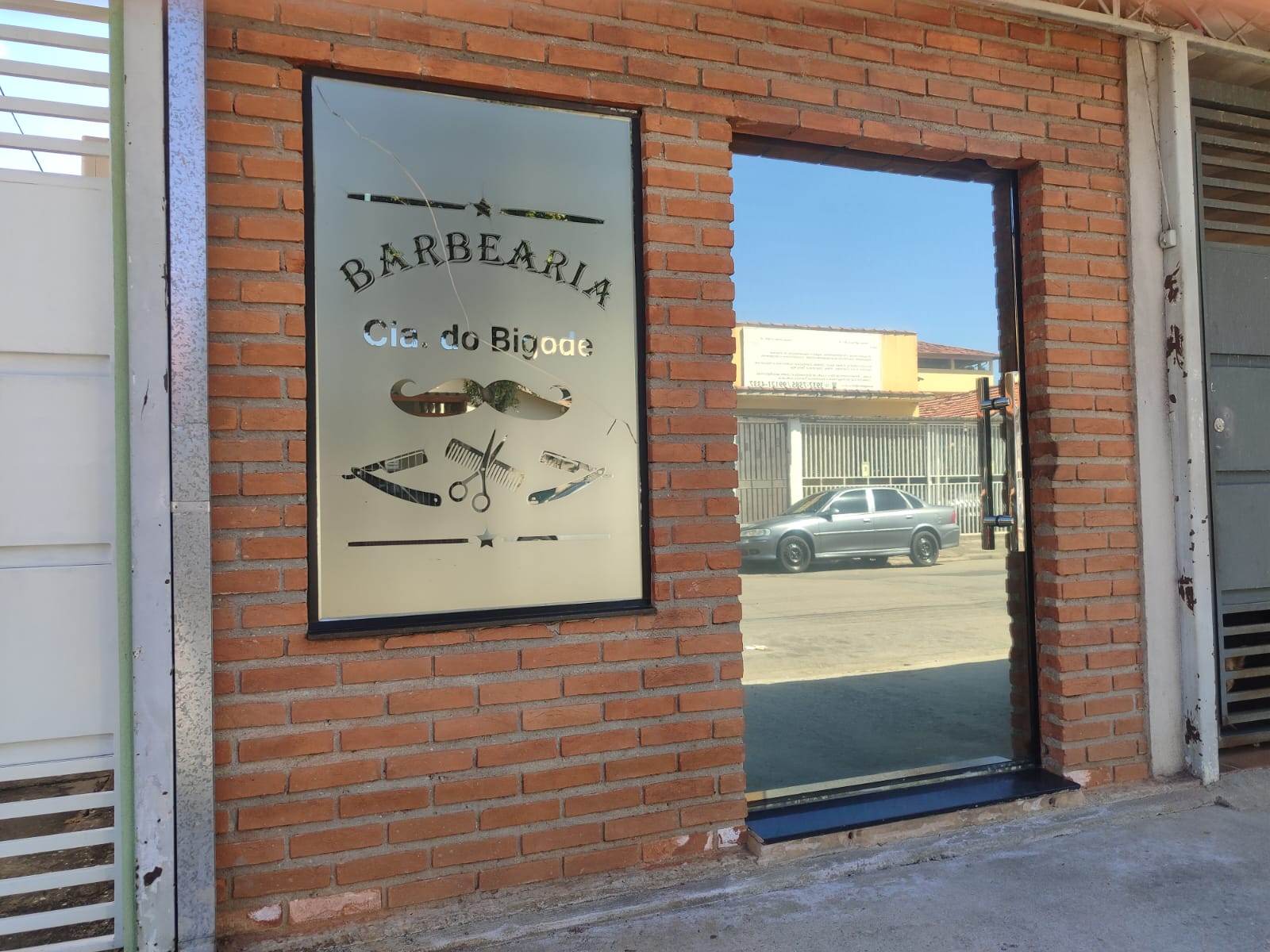 Fachada de tijolinho aparente da Barbearia Cia. do Bigode, com o letreiro gravado no vidro